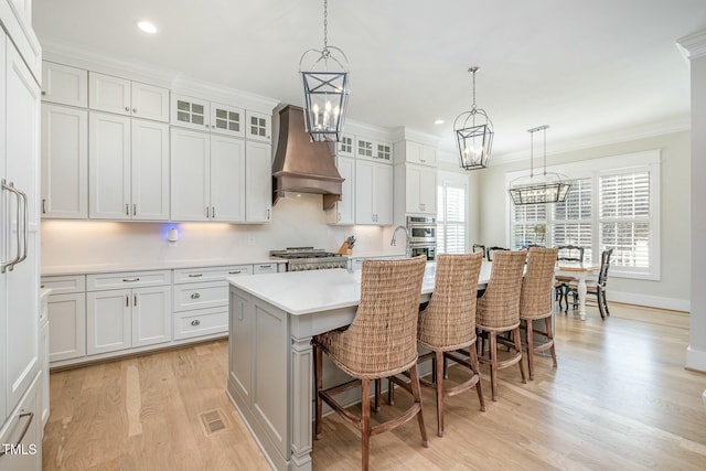 kitchen featuring a kitchen island with sink, a kitchen breakfast bar, light countertops, ornamental molding, and custom range hood