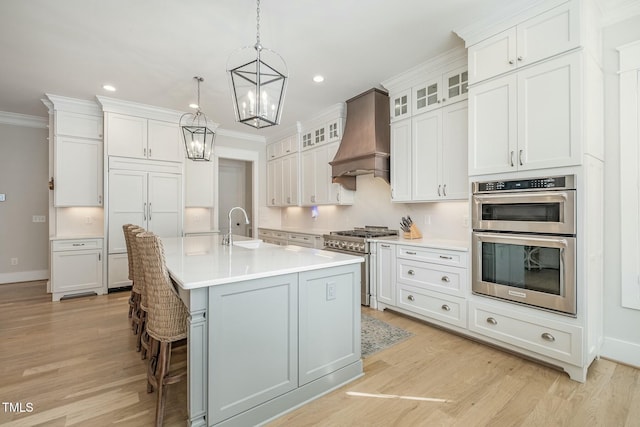 kitchen featuring appliances with stainless steel finishes, white cabinetry, an island with sink, sink, and custom exhaust hood