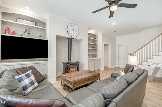 living room featuring ornamental molding, a wood stove, built in features, and light wood-type flooring