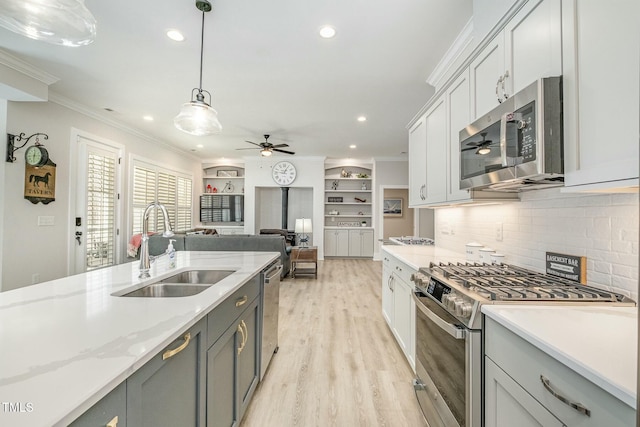 kitchen with light wood-style flooring, ornamental molding, stainless steel appliances, pendant lighting, and a sink