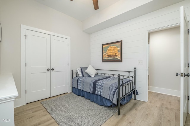 bedroom featuring ceiling fan, wooden walls, light hardwood / wood-style floors, and a closet