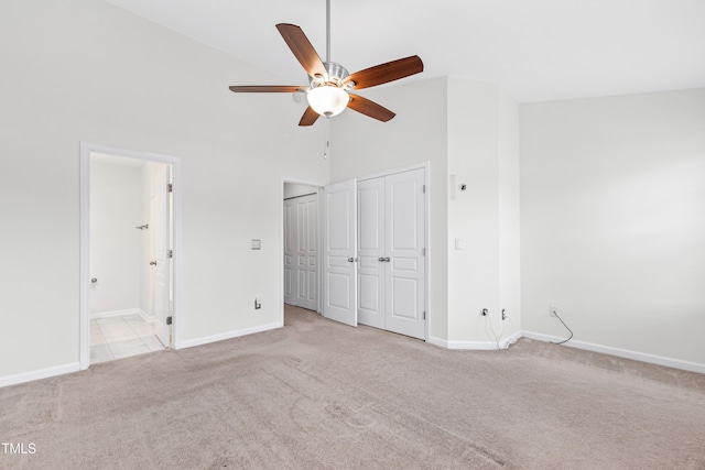 unfurnished bedroom with ceiling fan, high vaulted ceiling, ensuite bathroom, light carpet, and two closets