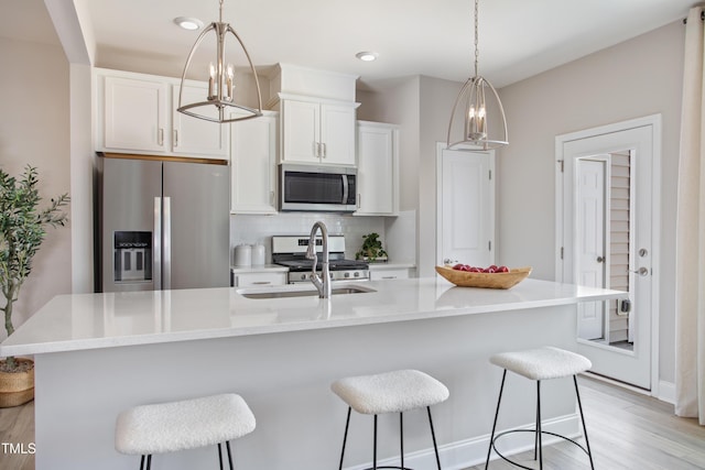 kitchen with appliances with stainless steel finishes, decorative light fixtures, white cabinetry, decorative backsplash, and a kitchen island with sink