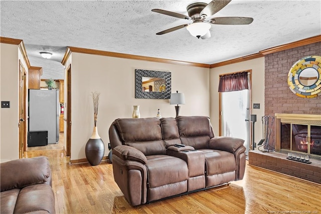 living room with crown molding, ceiling fan, a fireplace, light hardwood / wood-style floors, and a textured ceiling