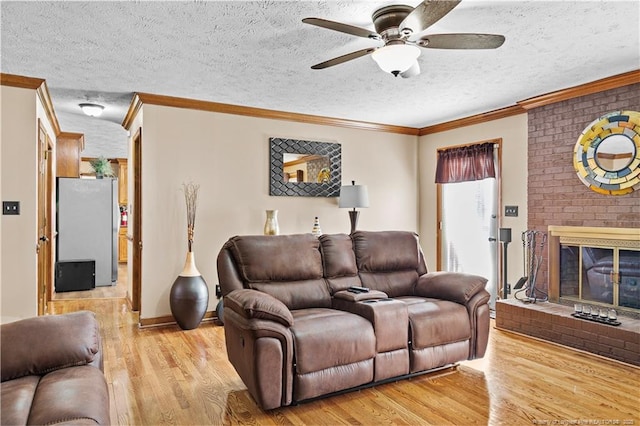 living room with a fireplace, ceiling fan, light hardwood / wood-style floors, crown molding, and a textured ceiling