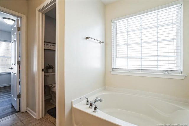 bathroom featuring toilet, plenty of natural light, tile patterned floors, and a tub to relax in