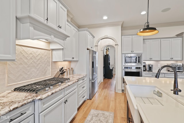 kitchen with decorative light fixtures, white cabinetry, sink, stainless steel appliances, and light wood-type flooring