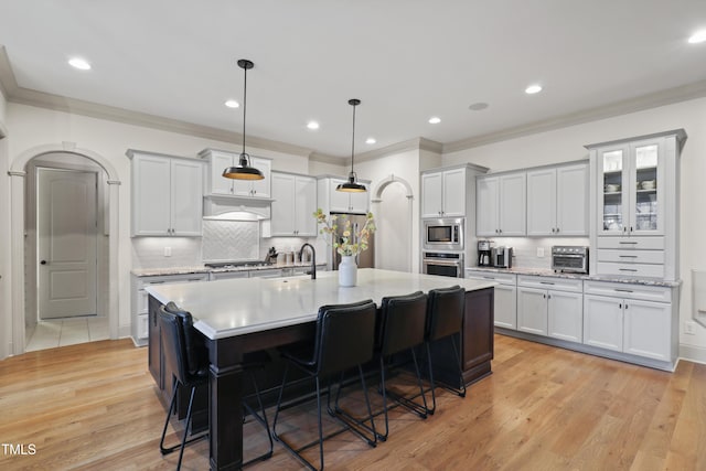 kitchen with a breakfast bar area, hanging light fixtures, stainless steel appliances, a kitchen island with sink, and white cabinets