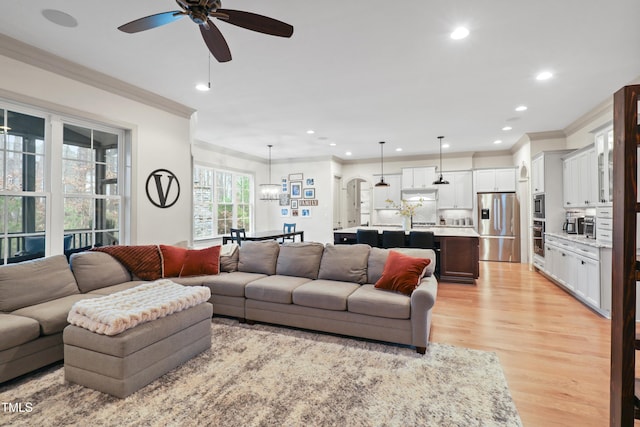 living room with ornamental molding, ceiling fan with notable chandelier, and light hardwood / wood-style flooring