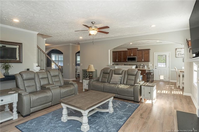 living room featuring ceiling fan, light hardwood / wood-style flooring, ornamental molding, and a textured ceiling