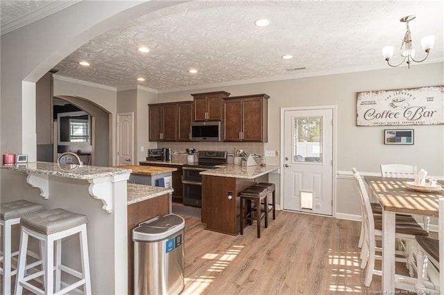 kitchen with appliances with stainless steel finishes, light stone counters, a kitchen breakfast bar, and kitchen peninsula