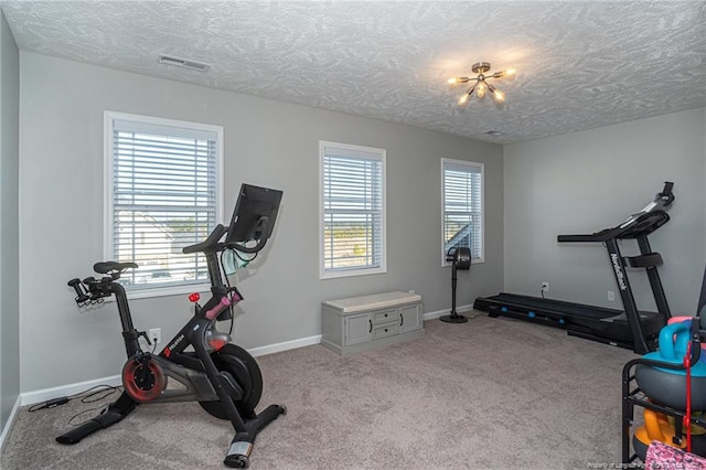 exercise room featuring an inviting chandelier, plenty of natural light, light carpet, and a textured ceiling