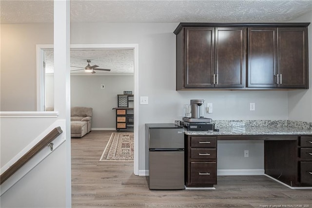 kitchen with dark brown cabinetry, hardwood / wood-style flooring, a textured ceiling, and light stone counters