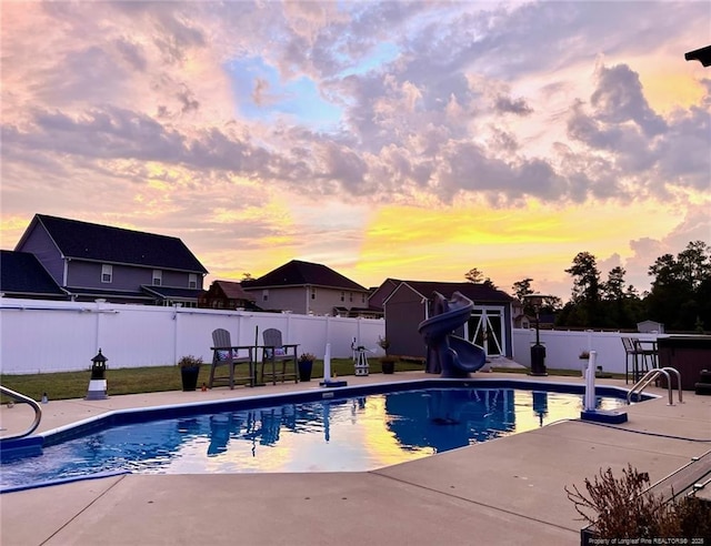 pool at dusk featuring a patio area and a water slide