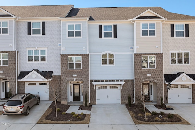 townhome / multi-family property with a garage, driveway, brick siding, and a shingled roof