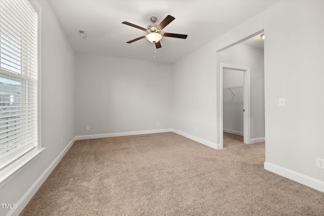 spare room with a ceiling fan, light colored carpet, a healthy amount of sunlight, and baseboards