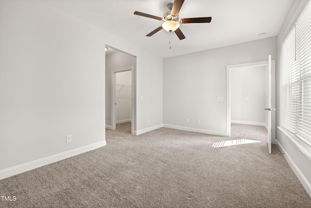 unfurnished bedroom with ceiling fan, a spacious closet, light colored carpet, and baseboards