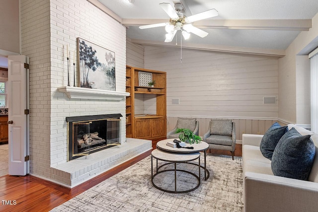 living room with hardwood / wood-style floors, wooden walls, a fireplace, lofted ceiling with beams, and ceiling fan