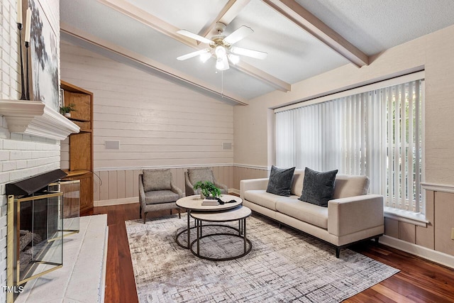 living room with ceiling fan, vaulted ceiling with beams, wooden walls, wood-type flooring, and a brick fireplace