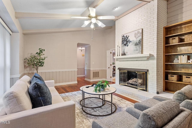 living room with vaulted ceiling with beams, a brick fireplace, built in features, ceiling fan, and light hardwood / wood-style floors