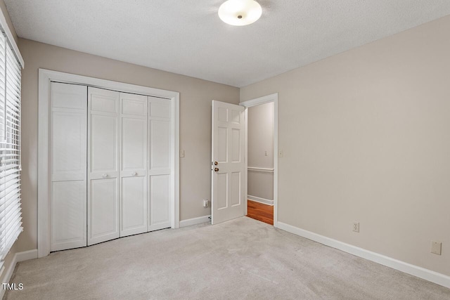 unfurnished bedroom featuring light colored carpet, a textured ceiling, and a closet