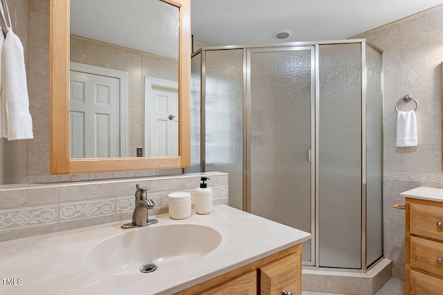 bathroom with vanity, a shower with door, and tile walls