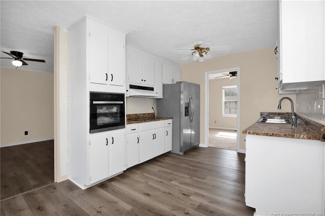 kitchen with sink, dark wood-type flooring, black oven, stainless steel fridge, and white cabinetry