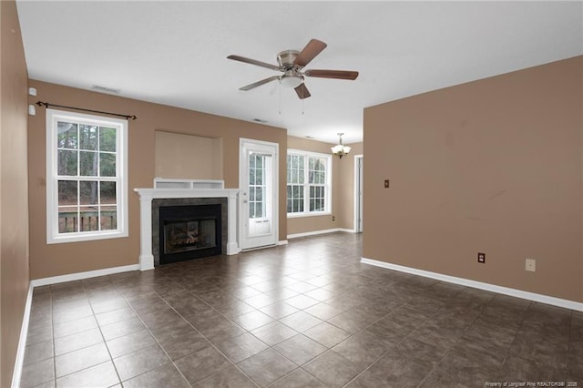 unfurnished living room with dark tile patterned flooring, ceiling fan with notable chandelier, and a wealth of natural light