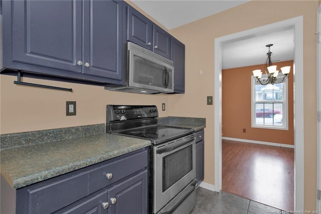 kitchen featuring stainless steel appliances, blue cabinets, dark tile patterned flooring, and a notable chandelier