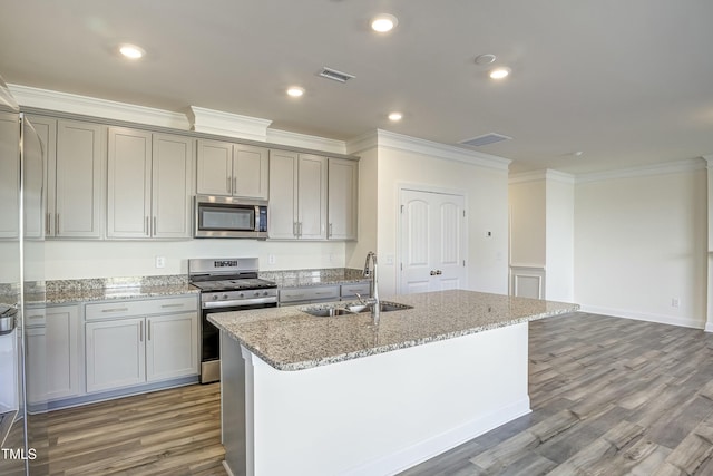 kitchen featuring stainless steel appliances, a kitchen island with sink, sink, and light stone countertops