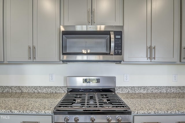 kitchen featuring light stone counters, stainless steel appliances, and gray cabinetry