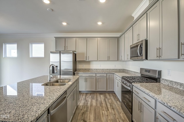 kitchen featuring sink, light stone counters, ornamental molding, appliances with stainless steel finishes, and light hardwood / wood-style floors