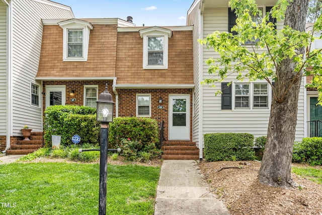 view of front facade featuring entry steps, a shingled roof, a front lawn, and brick siding