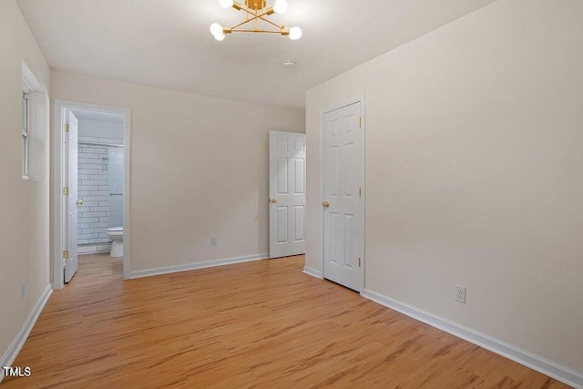 unfurnished bedroom with ensuite bath, a chandelier, and light hardwood / wood-style flooring