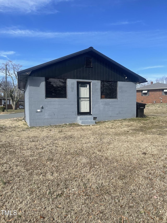 view of front of home with entry steps, concrete block siding, and a front lawn