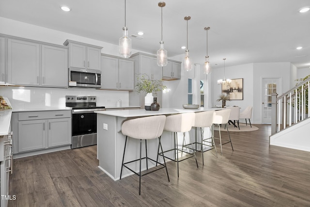 kitchen featuring a kitchen island, pendant lighting, gray cabinetry, a kitchen breakfast bar, and stainless steel appliances