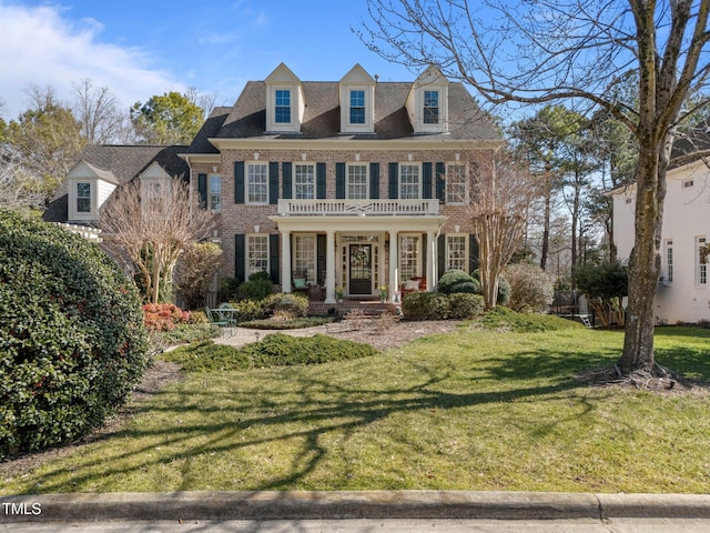 georgian-style home featuring a front lawn, a balcony, and brick siding