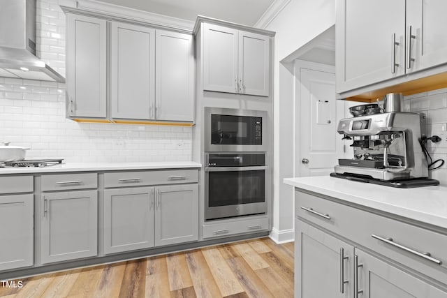 kitchen featuring backsplash, stainless steel appliances, light hardwood / wood-style floors, and wall chimney exhaust hood