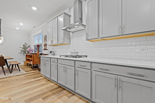 kitchen with gray cabinets, decorative backsplash, light hardwood / wood-style floors, crown molding, and wall chimney exhaust hood