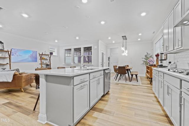 kitchen with dishwasher, an island with sink, sink, hanging light fixtures, and light hardwood / wood-style flooring