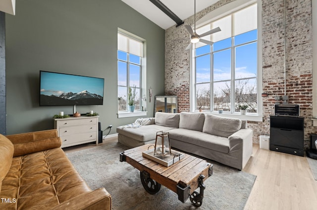 living room featuring beam ceiling, a towering ceiling, a wood stove, ceiling fan, and light wood-type flooring