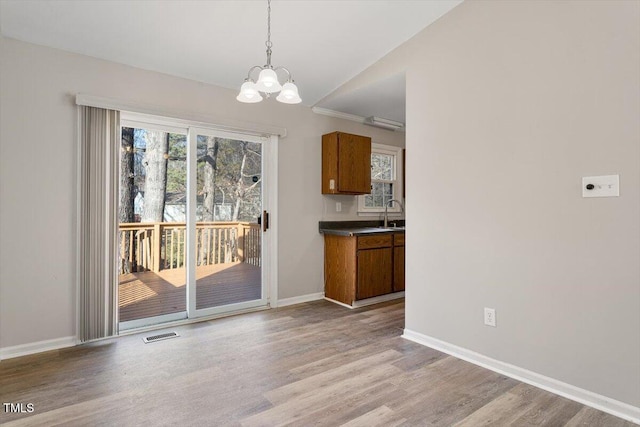 unfurnished dining area with lofted ceiling, sink, a chandelier, and light hardwood / wood-style floors