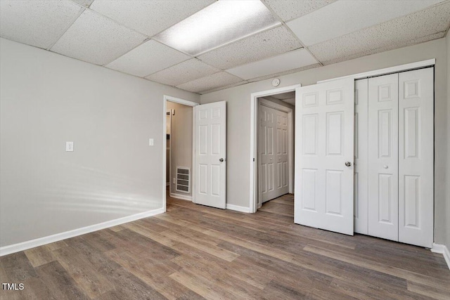 unfurnished bedroom with wood-type flooring, a closet, and a drop ceiling