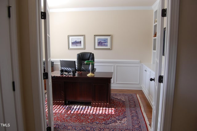 office space featuring a decorative wall, wainscoting, wood finished floors, and crown molding