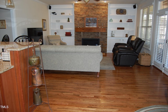 living area with a stone fireplace, dark wood-style flooring, built in features, and crown molding