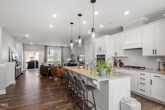 kitchen featuring a kitchen island with sink, hanging light fixtures, custom range hood, and white cabinets