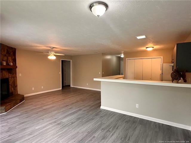 unfurnished living room with ceiling fan, a stone fireplace, wood-type flooring, and a textured ceiling