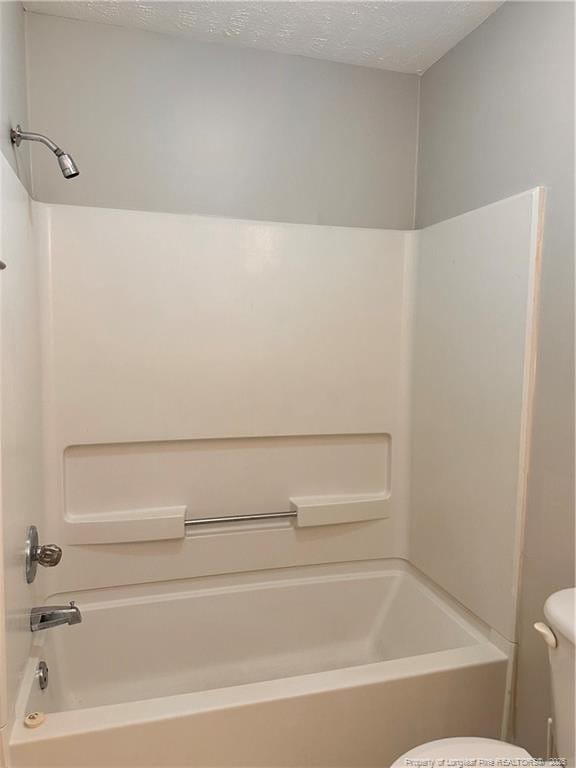 bathroom with bathing tub / shower combination, toilet, and a textured ceiling