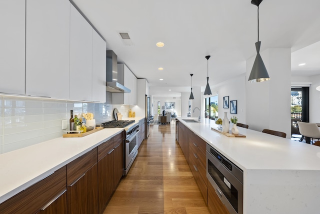 kitchen featuring sink, white cabinetry, pendant lighting, stainless steel appliances, and wall chimney range hood