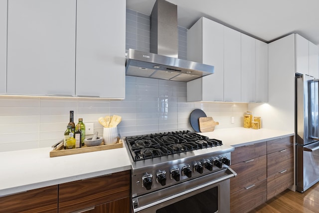 kitchen featuring tasteful backsplash, white cabinets, high end appliances, light wood-type flooring, and wall chimney exhaust hood